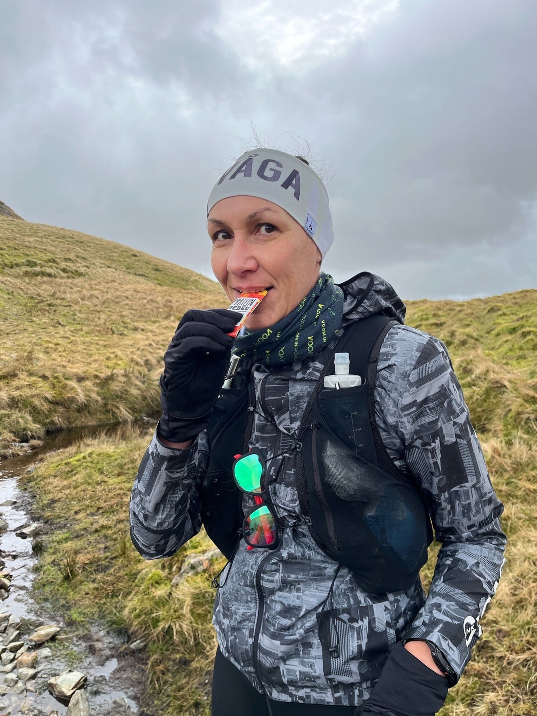 Nutritionist Zuzana standing by a stream during an ultra race with a Maple Ignite energy gel in her mouth