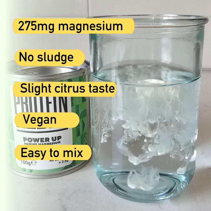tin of Power Up magnesium powder next to a glass of water on a worksurface. Power Up has been mixed into the glass of water showing how easily it dissolves