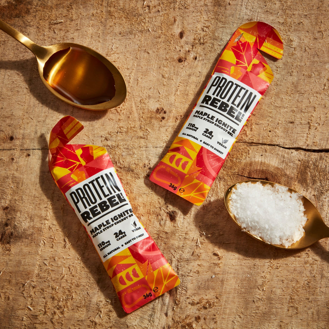 two packs of maple ignite on a wooden board with a gold dessert spoon of maple syrup and another gold dessert spoon of sea salt showing the two ingredients